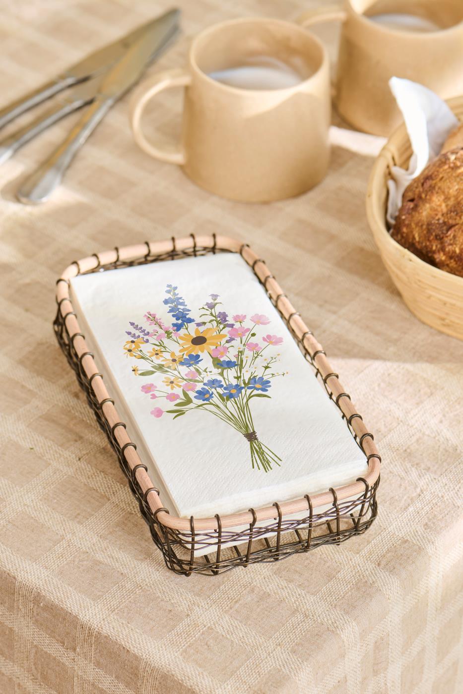 Servetten met bloemenprint in een mandje op een gedekte tafel met kopjes en brood