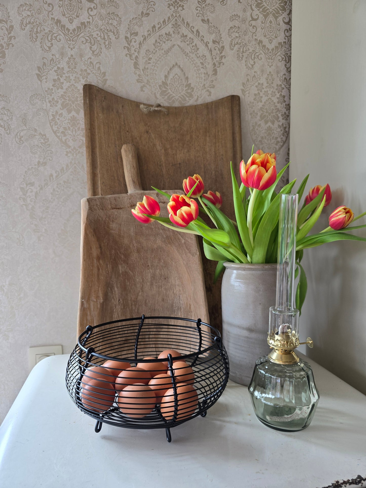 Zwart metalen eiermandje met bruine eieren op retro ijskast naast tulpen in vaas en olielamp