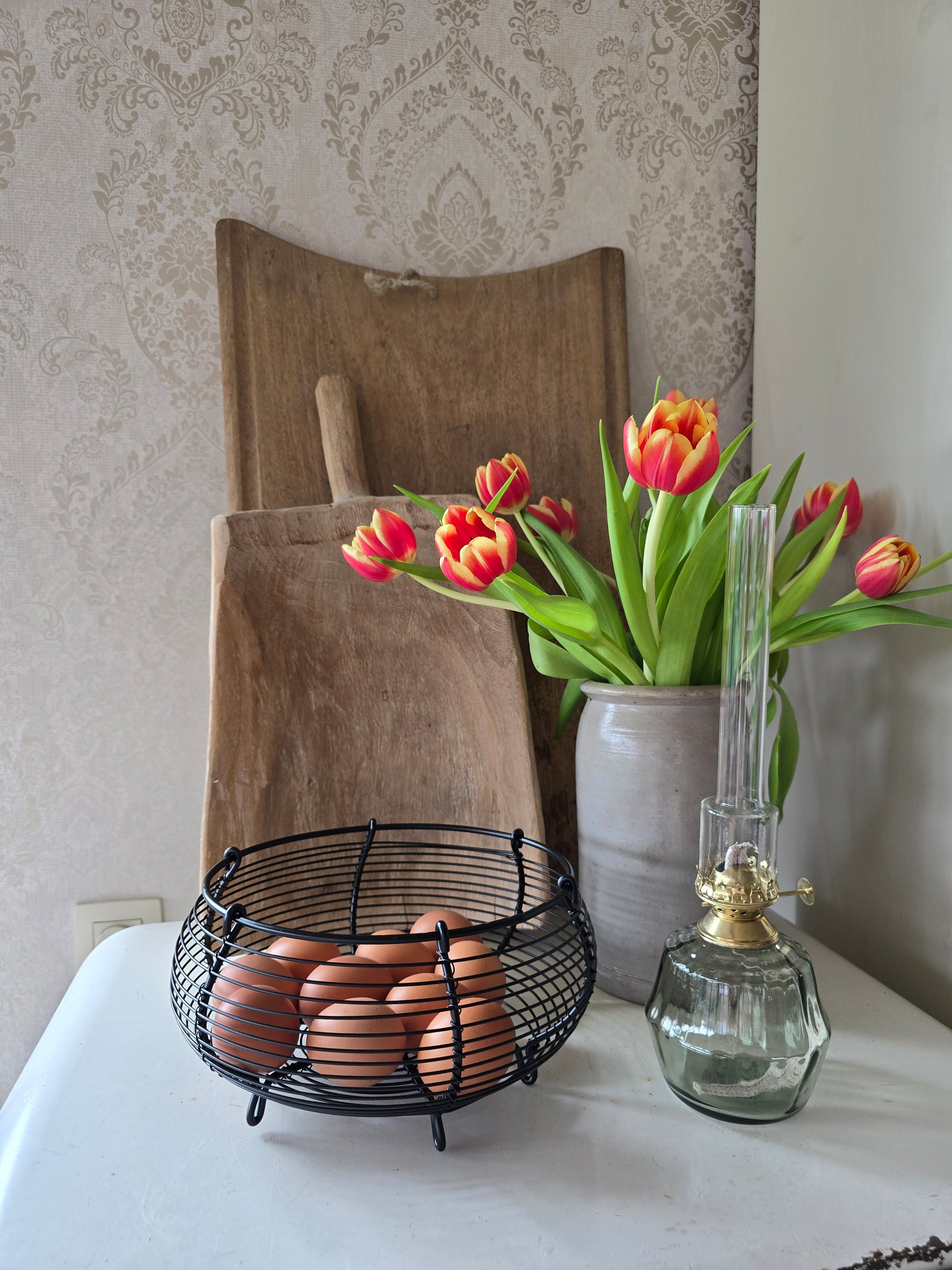 Zwart metalen eiermandje met bruine eieren op retro ijskast naast tulpen in vaas en olielamp